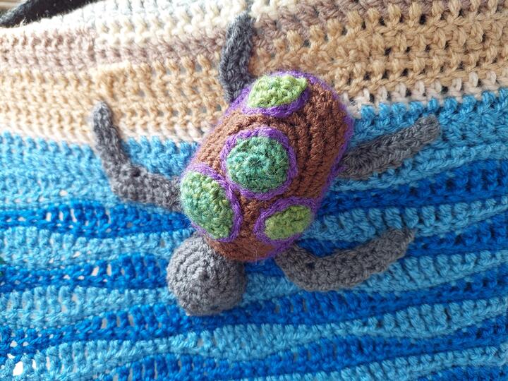 Crochet panel, created by Quakers working with the Loving Earth Project. Crochet turtle on a background of white and blue, suggesting the sea.