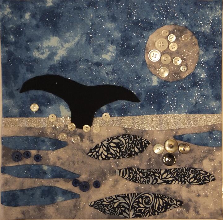 A glittery appliqued panel of a whale tail splashing up through an ocean underneath a moon, the moon and ocean spray are highlighted with pearlescent buttons.