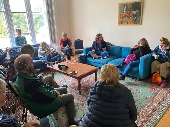 Wiston Weekend 2021 Zoe sitting cross-legged in a cozy room, in discussion with other Quakers