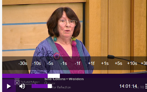 Sila at Parliament A woman stands before a microphone at the Scottish Parliament, delivering a speech